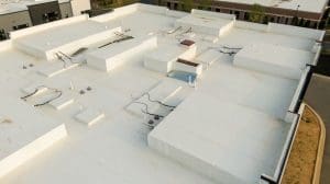 Aerial drone inspection of commercial TPO roof featuring heat-welded seams HVAC curb flashing and pipe penetrations - Oak Grove Roofing - Oak Grove Roofing Overhead view of a flat white commercial rooftop with rectangular roof structures and scattered cables