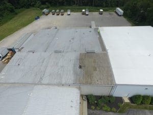 DCIM100MEDIADJI_0014JPG - Oak Grove Roofing - Oak Grove Roofing Aerial view of a warehouse with flat metal roofs and a row of trucks parked along the edge of a paved lot.