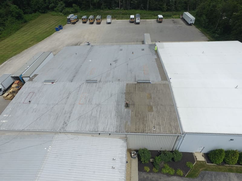 Aerial view of a warehouse with flat metal roofs and a row of trucks parked along the edge of a paved lot.