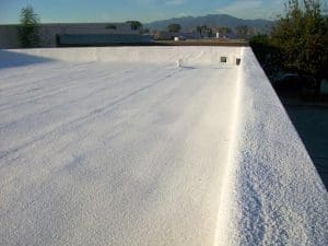 Spray-Foam-Roofing-Lancaster-PA-Pennsylvania-2 - Oak Grove Roofing - Oak Grove Roofing White flat roof with a textured, bright coating and a low parapet, mountains in the distance.