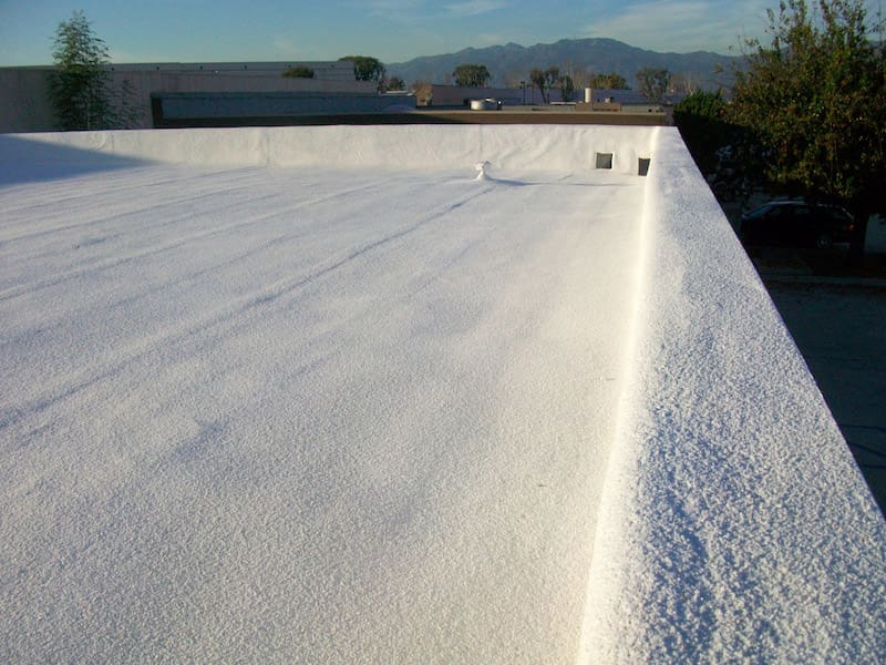 White flat roof with a textured, bright coating and a low parapet, mountains in the distance.
