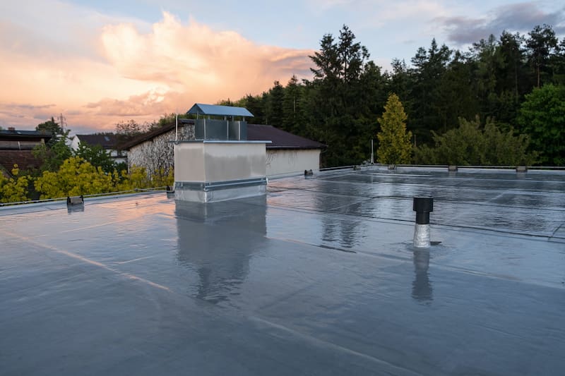 Flat roof covered with bitumen membrane and silver lacquer with chimney on a private house Reflections after rain - Oak Grove Roofing